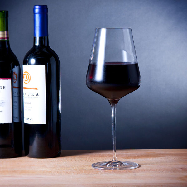 A wine bottle and glass of Stolzle Bordeaux wine on a table.
