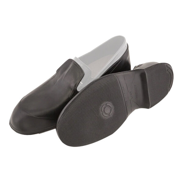 A close-up of a large black Tingley rubber overshoe on a white sole.