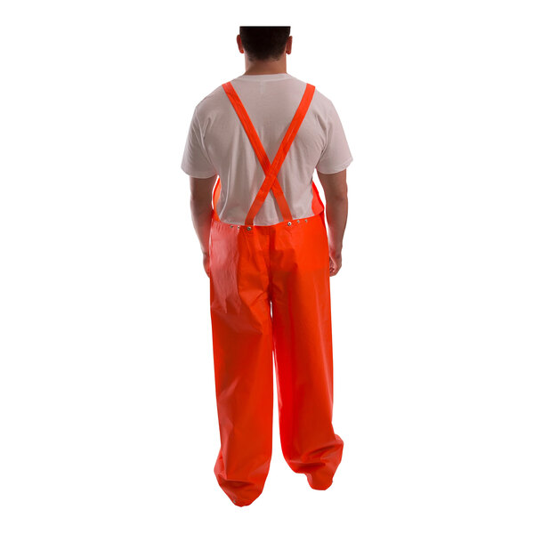 A person wearing an orange Tingley rainsuit with suspenders.