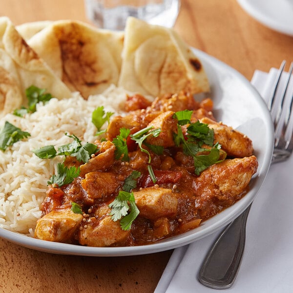 A white plate of chicken curry with rice and bread with a fork and knife next to it.