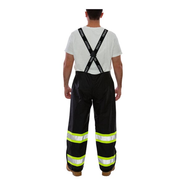 A man wearing Tingley black overalls with black suspenders over a white shirt.