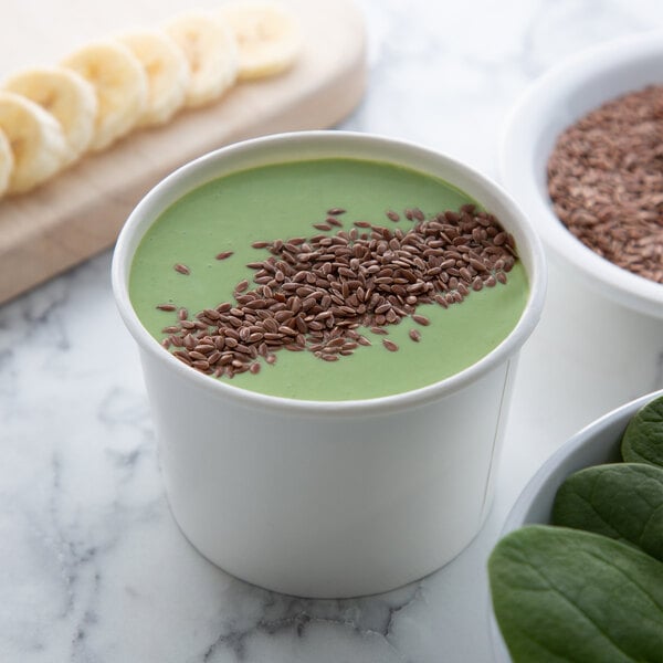 A bowl of green smoothie with flax seeds and banana slices on a counter with a bowl of brown flax seeds.