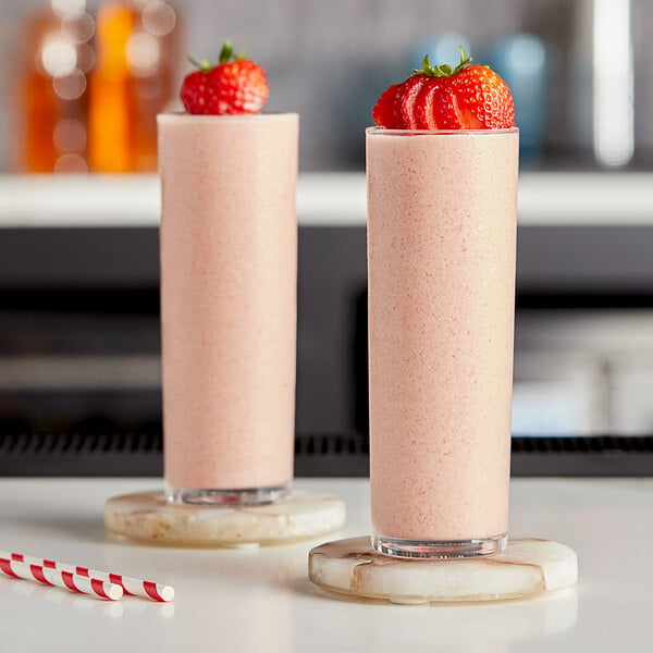 Two glasses of pink strawberry slushies with straws.