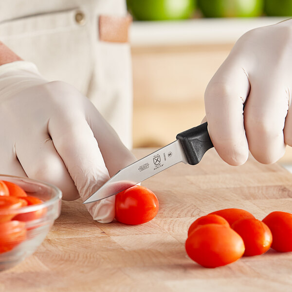 A person in white gloves using a Mercer Culinary Millennia clip point paring knife to cut a tomato on a cutting board.