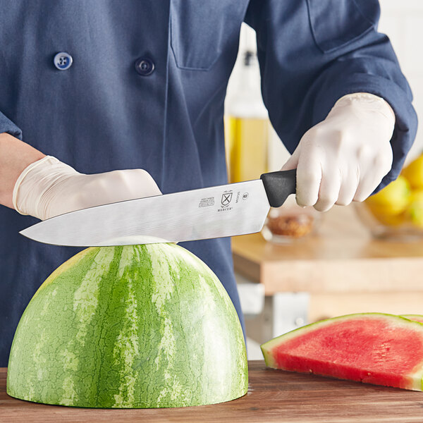 A person using a Mercer Culinary chef knife to cut a watermelon.