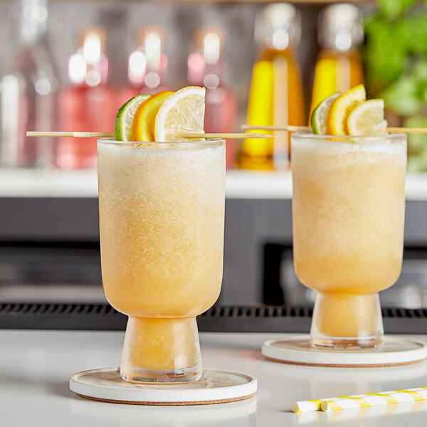 Two glasses of organic frozen citrus cocktails with lemon and lime slices and straws.