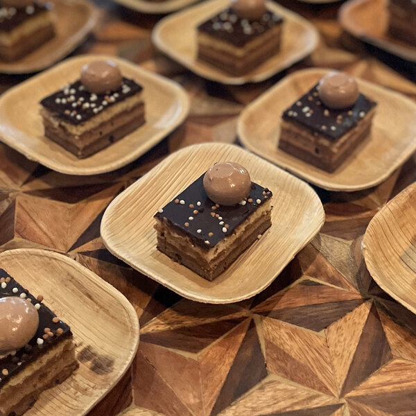 A VerTerra square palm leaf plate with small square desserts topped with chocolate and nuts.