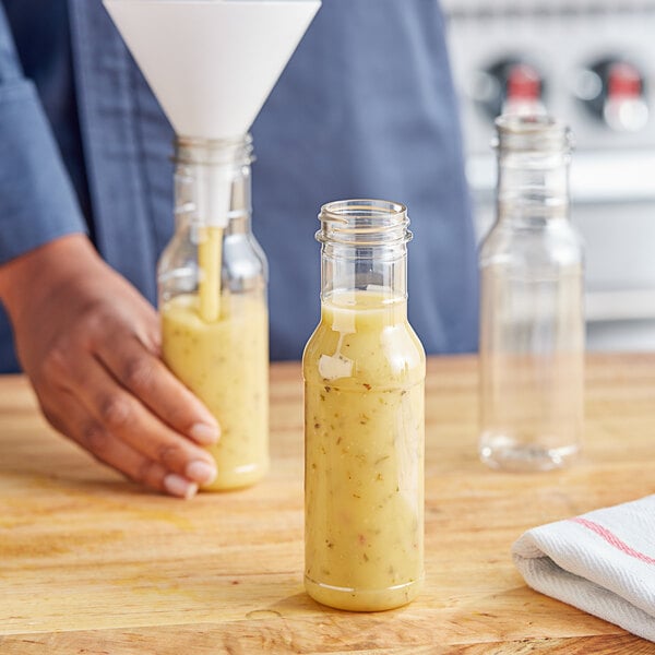 A hand pouring yellow liquid into an 8 oz. PET Ring Neck Sauce Bottle.