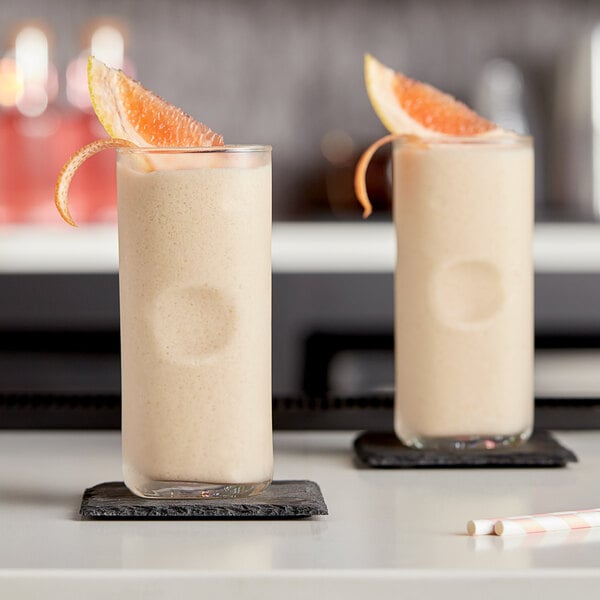 Two glasses of grapefruit slushies with orange slices on a table.