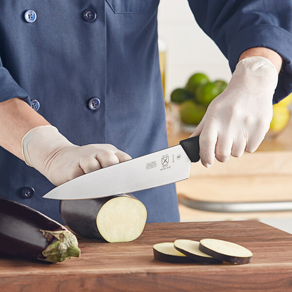 A person in a chef's uniform cutting eggplant with a Mercer Culinary chef knife.