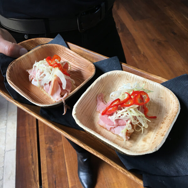 A person holding a tray of VerTerra wooden bowls filled with food.