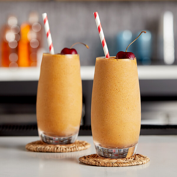 A close up of two glasses of orange frozen cocktails with straws.