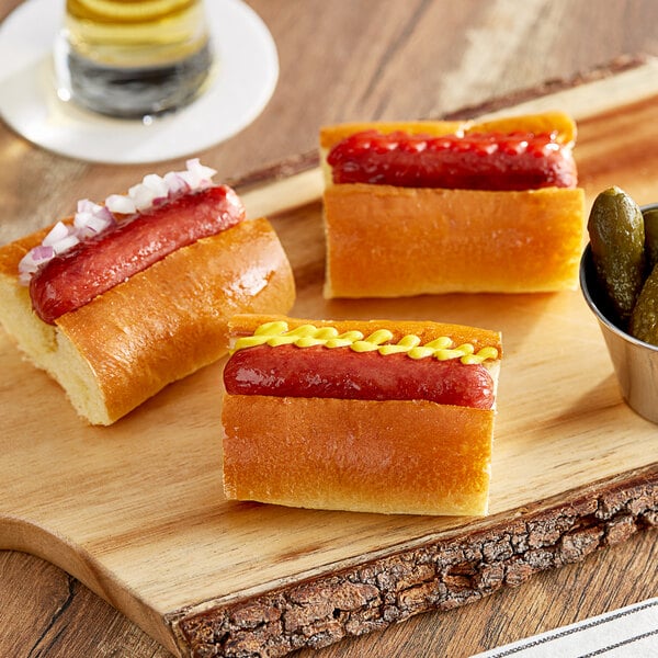 Vienna Beef mini hot dogs on a cutting board with pickles.