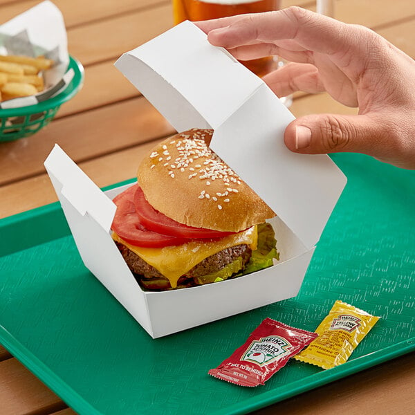 A hand holding a burger in a white paper take-out box.