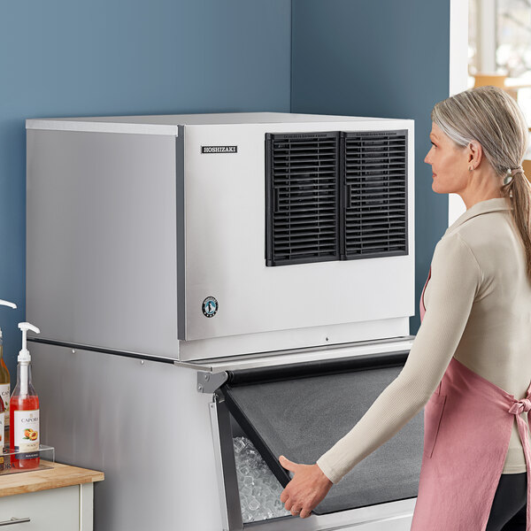 A woman in an apron opening a large Hoshizaki air cooled ice machine.