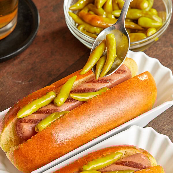 Two hot dogs with Chipico sport peppers and mustard on a plate.
