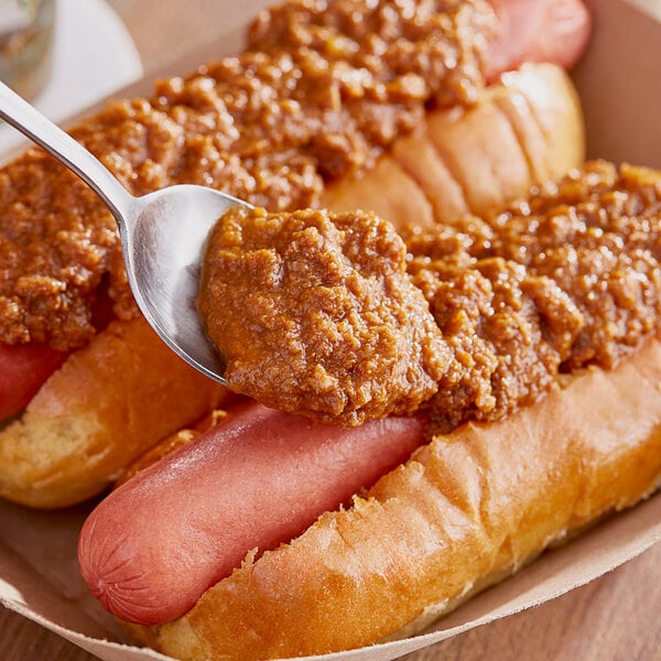 Two Vienna Beef chili dogs on a table with a spoon of red chili sauce.