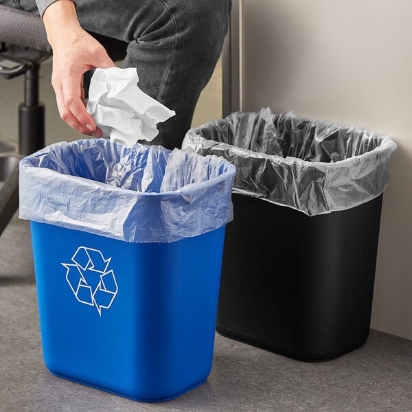 A man's hand throws a crumpled white paper towel into a blue Lavex rectangular trash can.