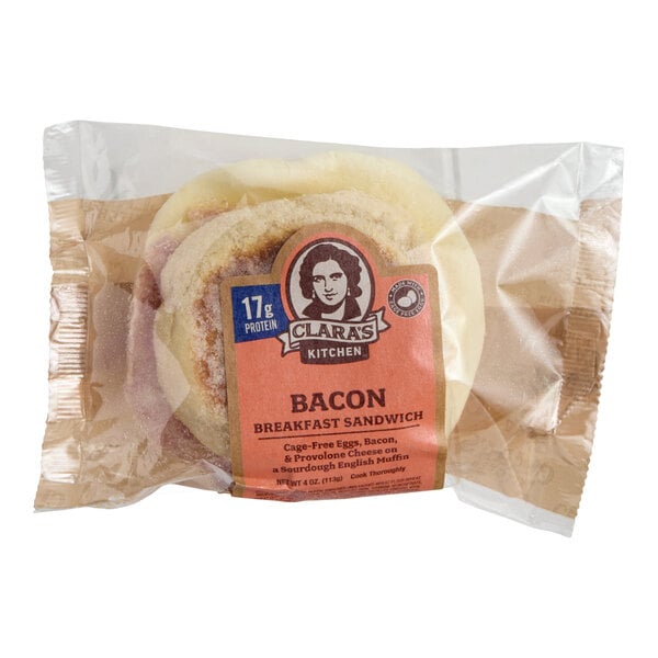 A packaged Clara's Kitchen Bacon Breakfast Sandwich featuring cage-free eggs, bacon, and provolone cheese on a sourdough English muffin.