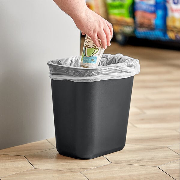 A hand putting paper into a black Lavex rectangular wastebasket.