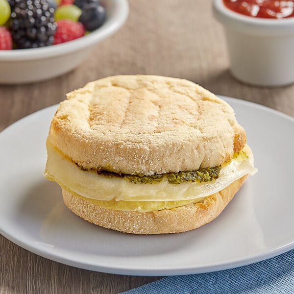 A Clara's Kitchen breakfast sandwich with cheese and pesto on a plate with fruit.