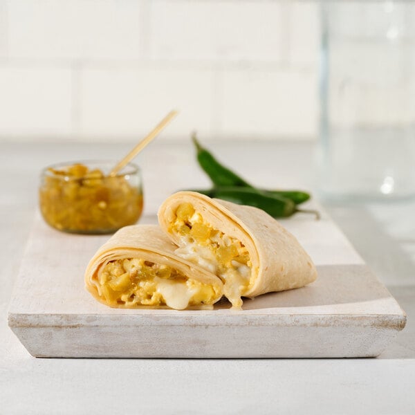 A breakfast burrito filled with chile verde, eggs, and cheese, cut in half and displayed on a white board.