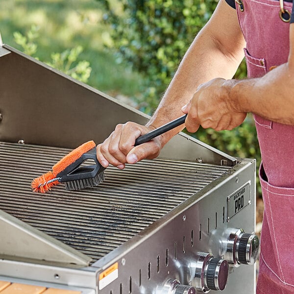 A man using a Mr. Bar-B-Q grill brush to clean a grill.