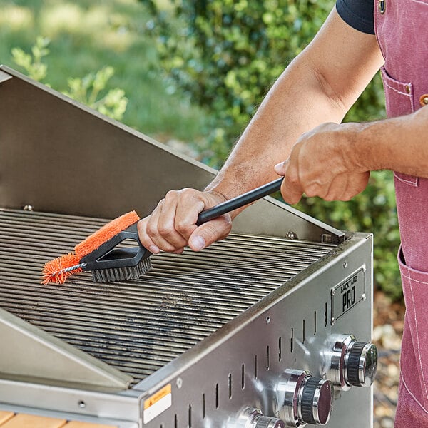 A person cleaning a grill with a Mr. Bar-B-Q Triple-Action Grill Brush.
