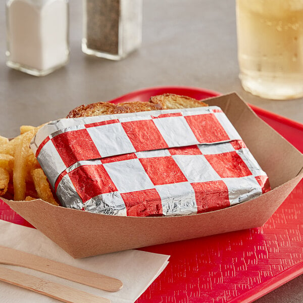 A sandwich and fries wrapped in red and silver checker foil on a tray.