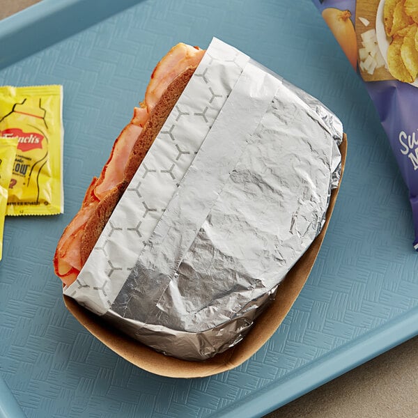 A Bagcraft silver honeycomb foil wrapped sandwich on a tray.