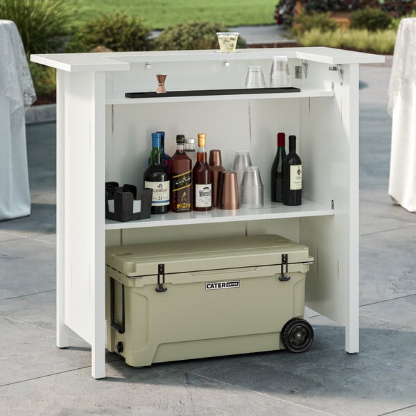 A white Lancaster Table and Seating portable bar with bottles and a cooler on the shelf.