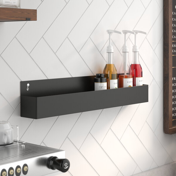 A Steelton black single tier speed rail on a counter holding bottles of liquid.