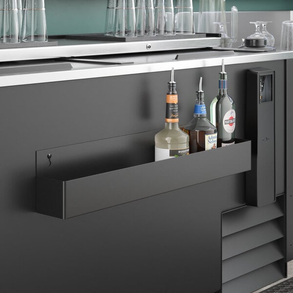 A Steelton black single tier speed rail on a counter with bottles of liquor and glasses.