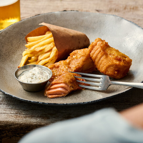 A plate of vegan salmon filets served with French fries and a side of dipping sauce.