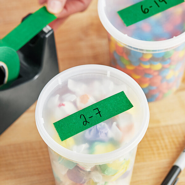 A hand using Lavex green masking tape to label a plastic container of candy.