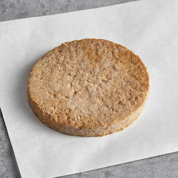 A round brown Before the Butcher vegan sausage patty on a white surface.