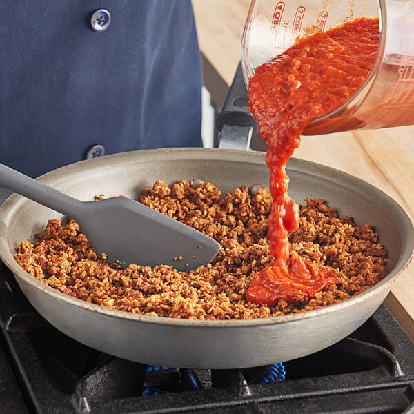 A person pouring red sauce into a pan of Before the Butcher Plant-Based Vegan Ground Sausage.