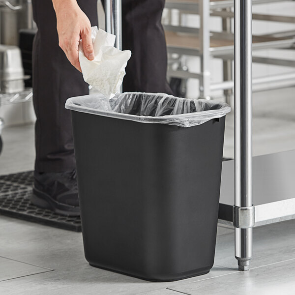 A person putting a paper towel in a black Lavex rectangular trash can.