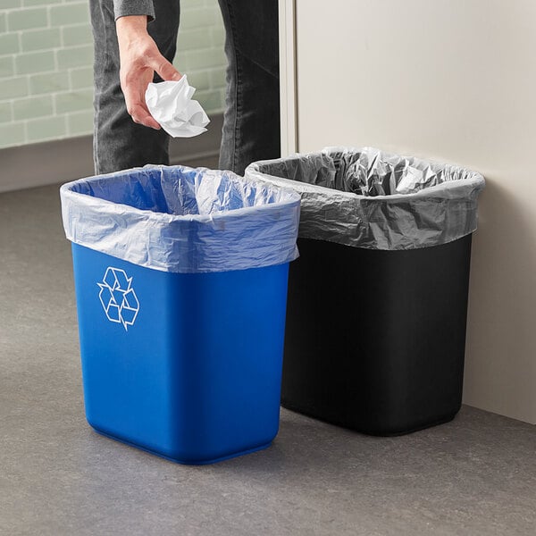 A man throwing a crumpled paper into a black and blue Lavex rectangular trash can.