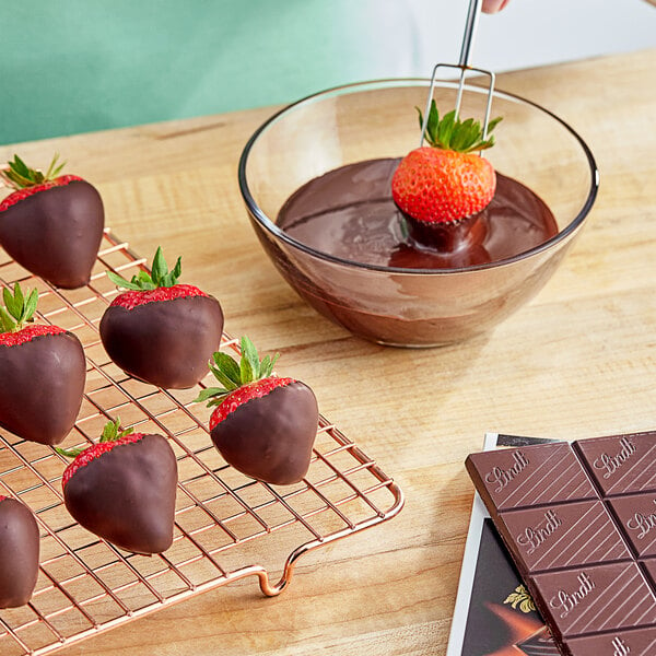 A strawberry being dipped into a bowl of dark chocolate.