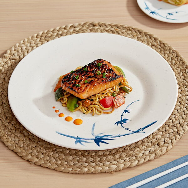 A Bambu Biru melamine plate with food on it sits on a table with a woven mat underneath.