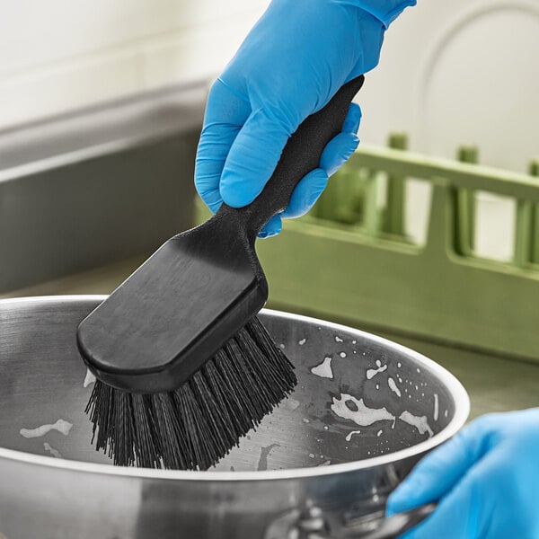 A person in blue gloves using an Advantage Supplies black floating utility/pot scrub brush to clean a pan.