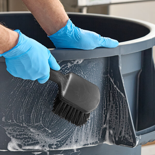 A person using an Advantage Supplies black floating utility brush to clean a bucket.