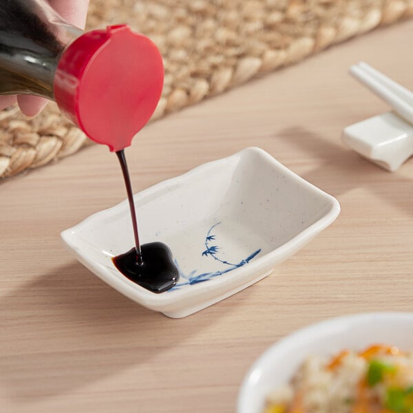 A person pouring soy sauce into a small white rectangular bowl.