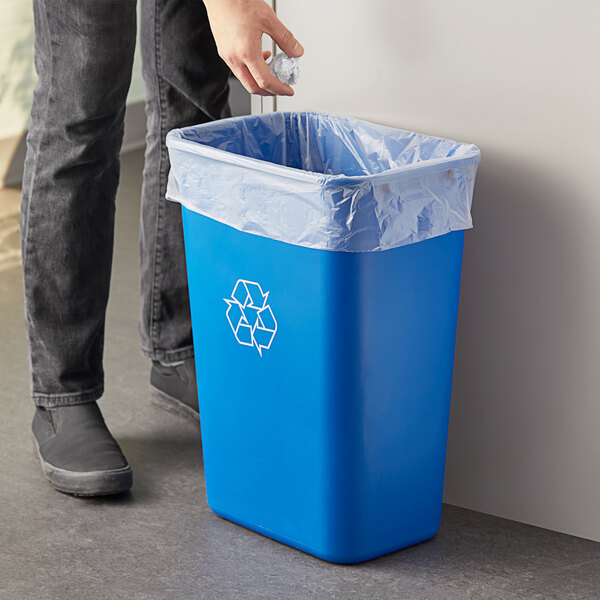 A person putting a plastic bag into a blue rectangular Lavex recycling bin.