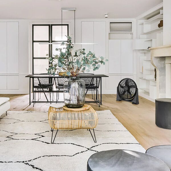 A VisionAir black air circulator in a white room with a black chair and a vase of flowers.