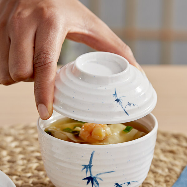 A hand holding an Acopa Bambu Biru melamine bowl with a lid.