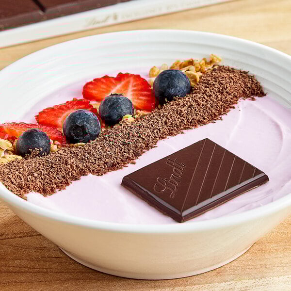 A bowl of yogurt with strawberries, blueberries, and Lindt dark chocolate.