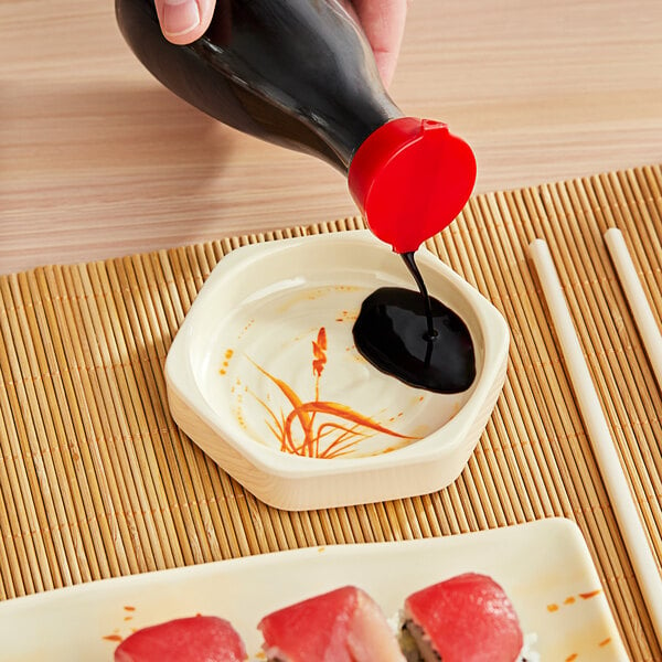 A hand pouring sauce into a bowl of sushi on a table.