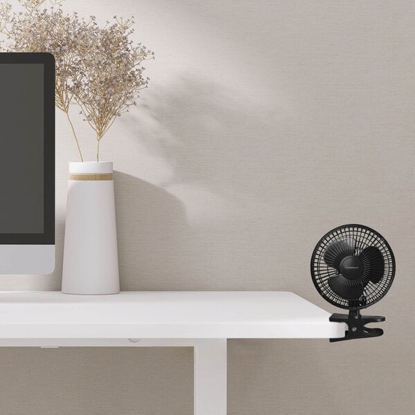 A black VisionAir desk fan on a white desk.